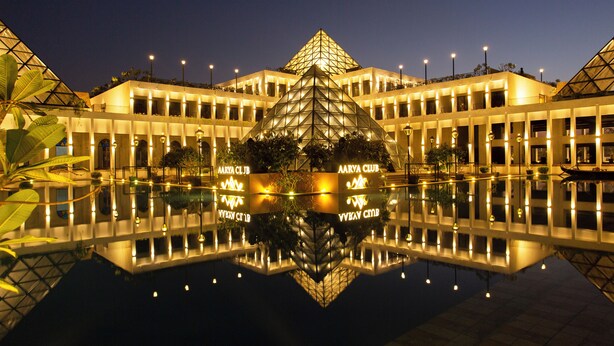 Un hotel amb una estructura piramidal central, nombroses plantes i una piscina reflectant.