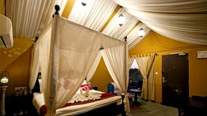 Habitació amb un llit sota una bugenvila, una taula de nit, una làmpada i una porta.