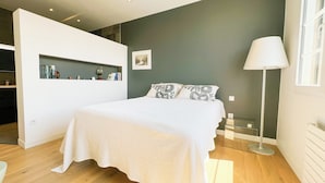 Une chambre à coucher moderne avec un lit, une lampe de chevet, une étagère murale avec des livres et un tableau.