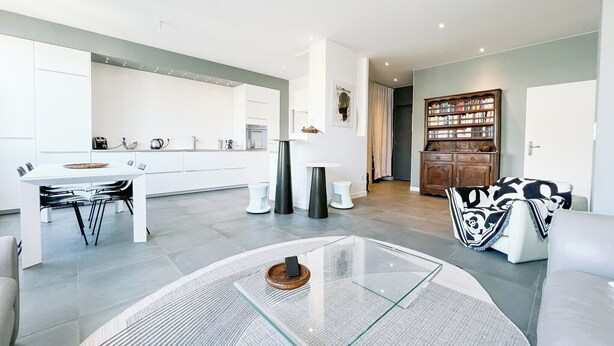 Une cuisine moderne avec des meubles blancs, une table à manger avec des chaises, une table basse ronde en verre et une bibliothèque.