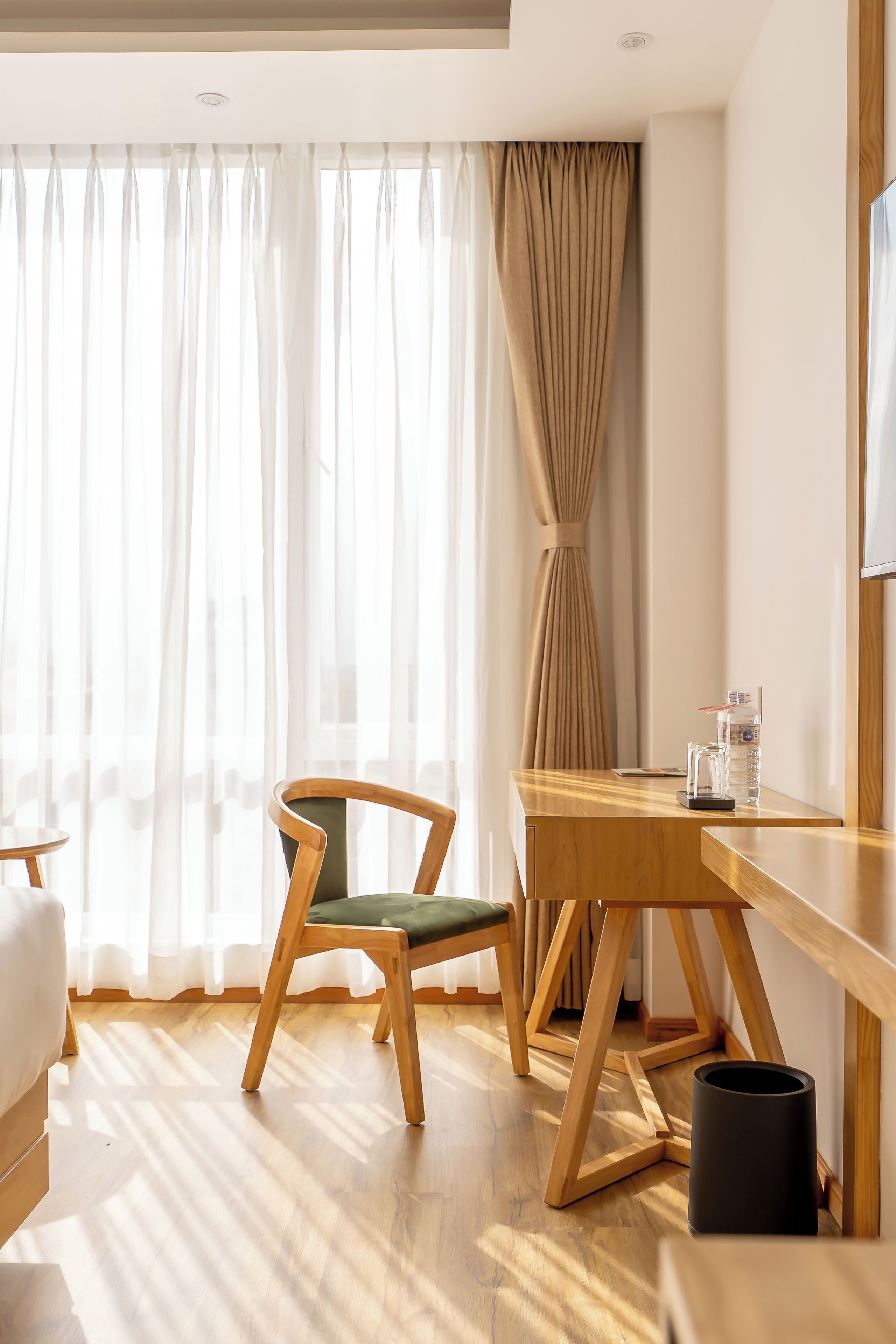 A modern room with a wooden desk, a chair, and a large window with sheer curtains.