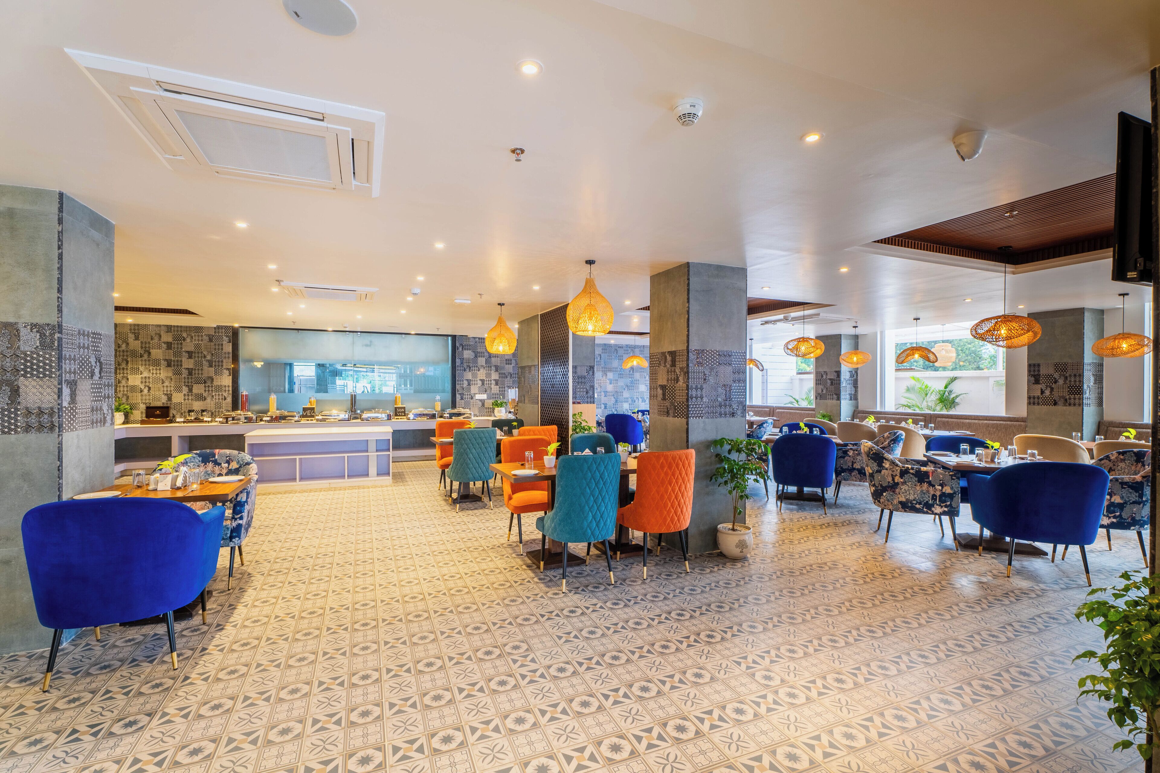 Un restaurant spacieux doté d’un sol à motifs, de plusieurs espaces de restauration avec des chaises colorées et d’un éclairage suspendu.