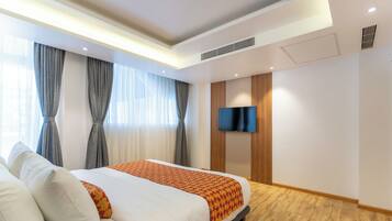 A hotel room with a bed, a TV, and a wooden floor.