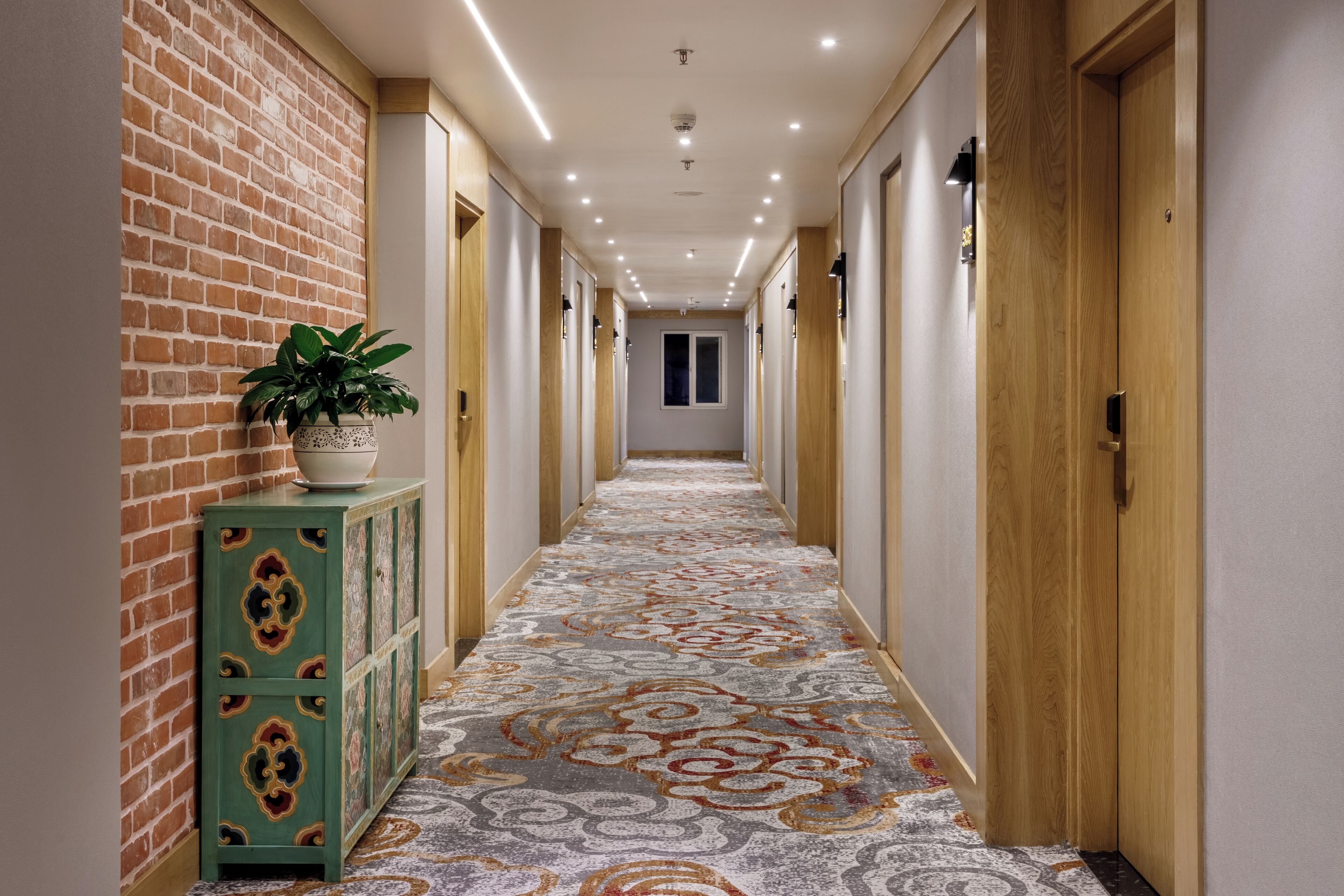 Un pasillo con alfombra estampada, puertas de madera y pared de ladrillo.