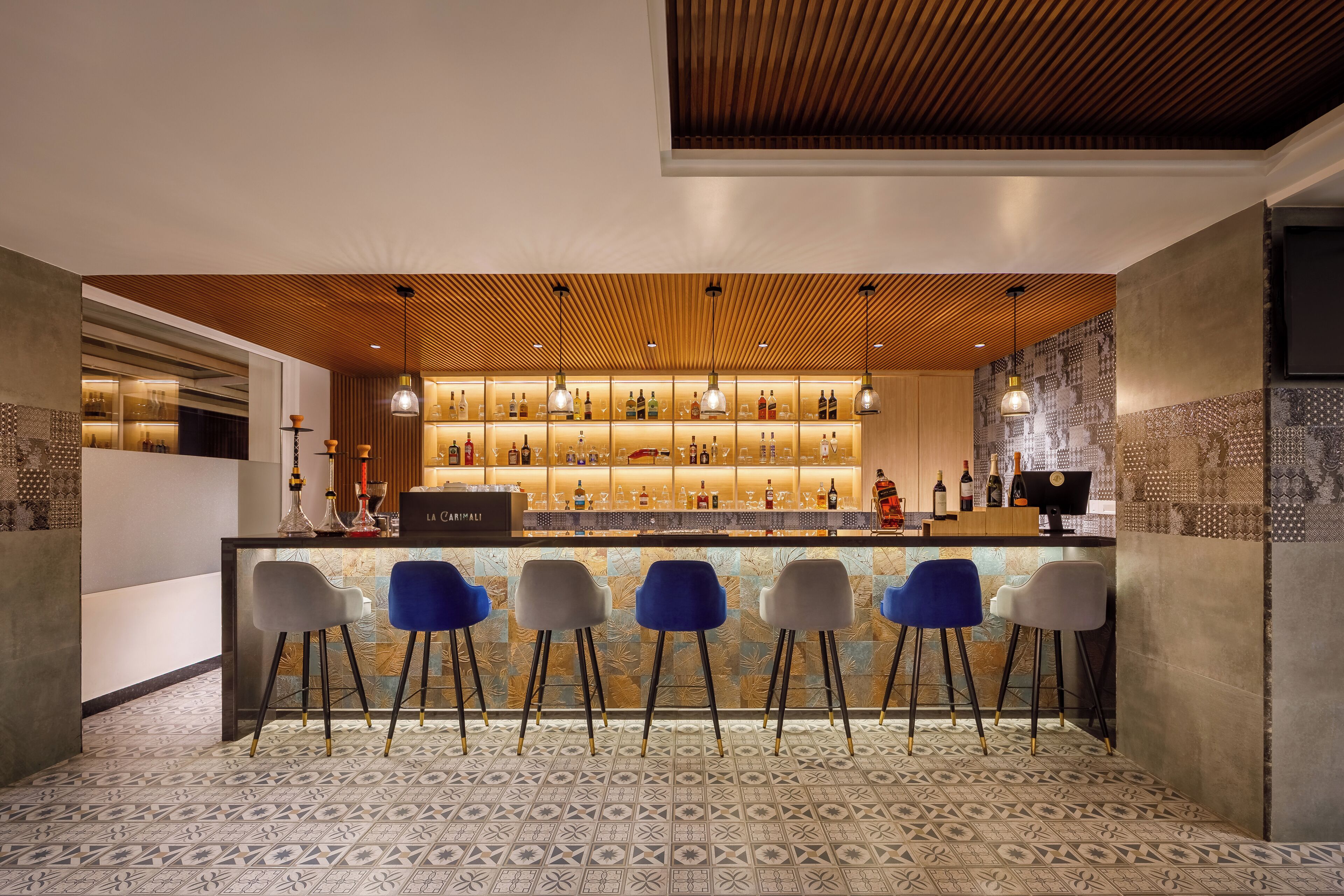 A bar area with a wooden ceiling, a patterned floor, and bar stools.