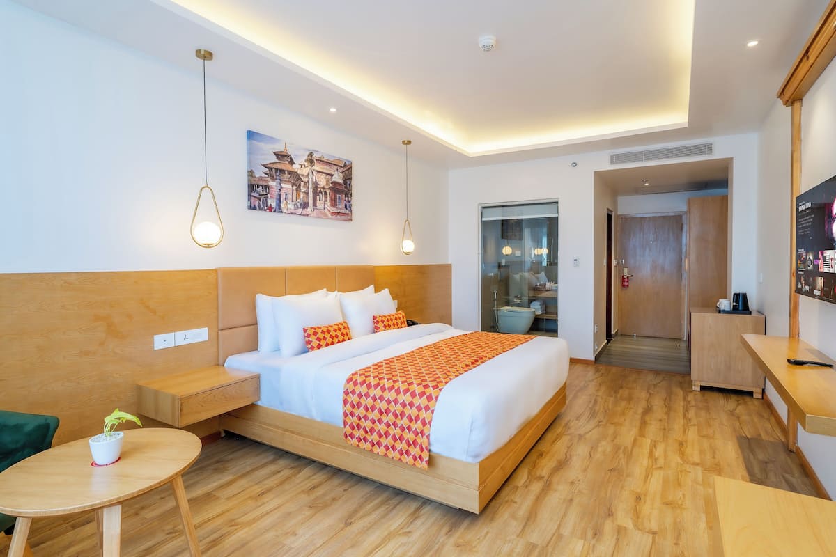 A modern hotel room with a wooden bed, a small table with a plant, and a painting on the wall.