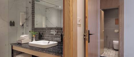 Un baño moderno con lavamanos de mármol, cabina de ducha de vidrio y tocador de madera.