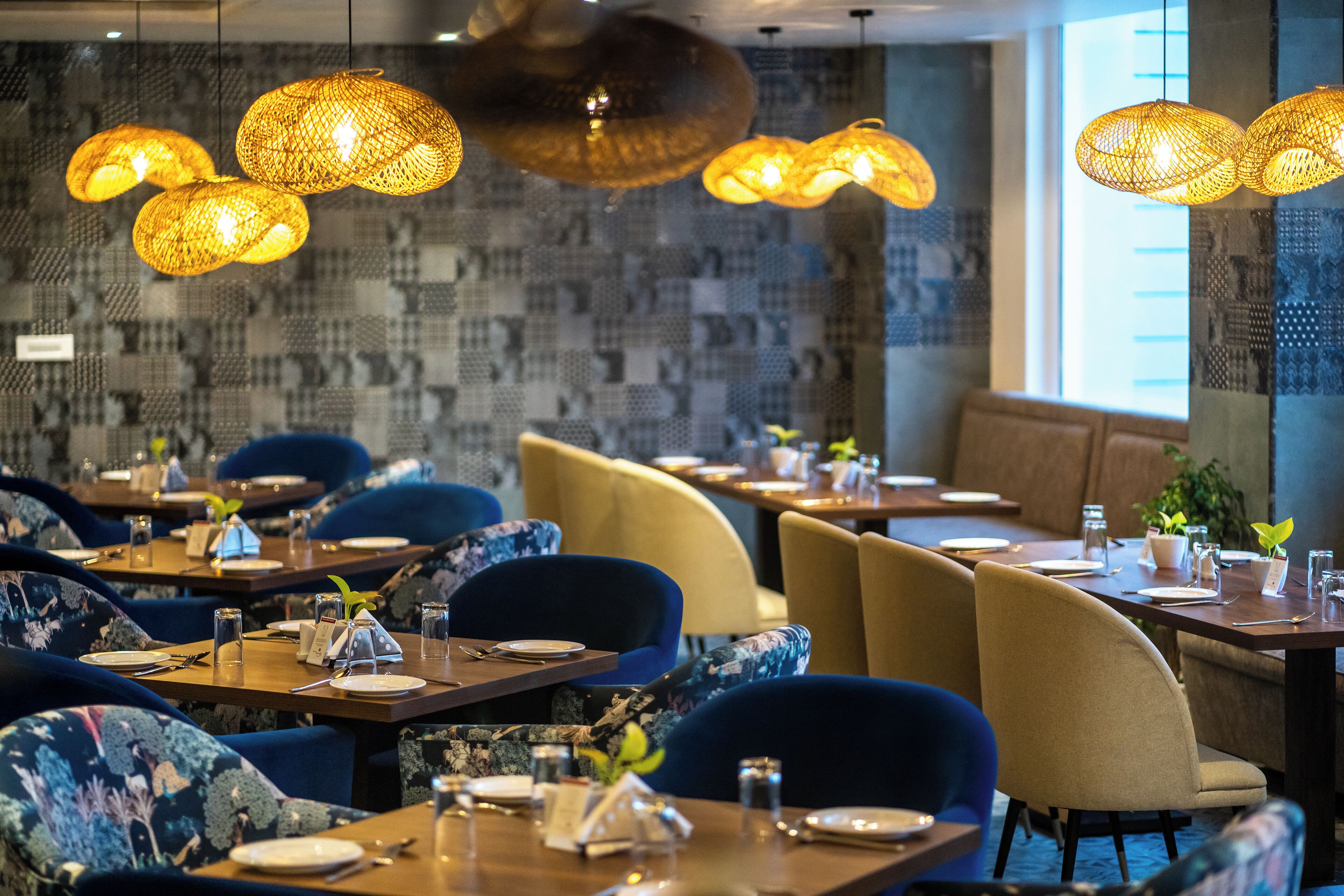 Ein Restaurant mit gedeckten Tischen, blau und beige Stühlen und hängenden Korblampen.