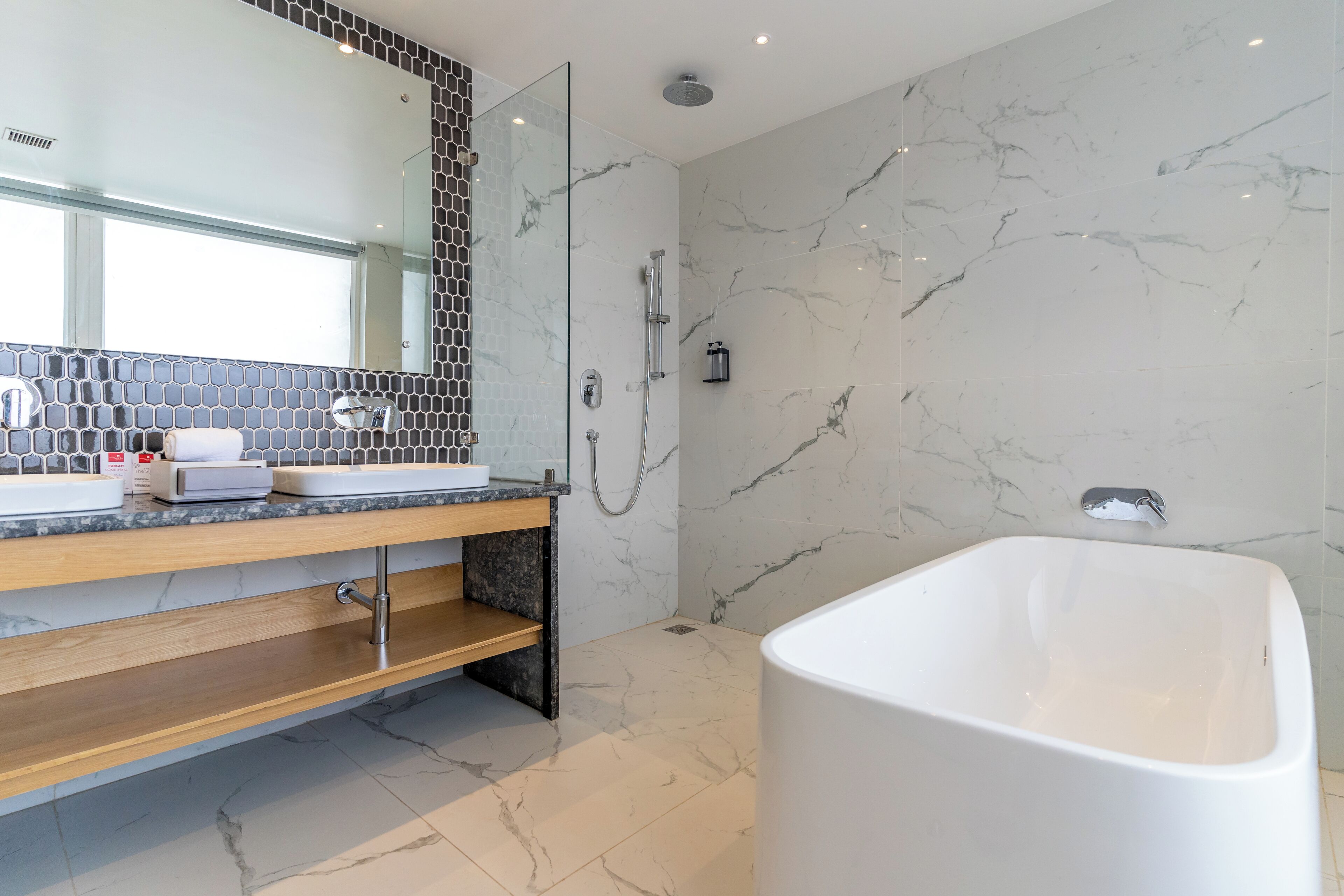 A modern bathroom with a freestanding bathtub, a glass-enclosed shower, and a vanity with a marble backsplash.