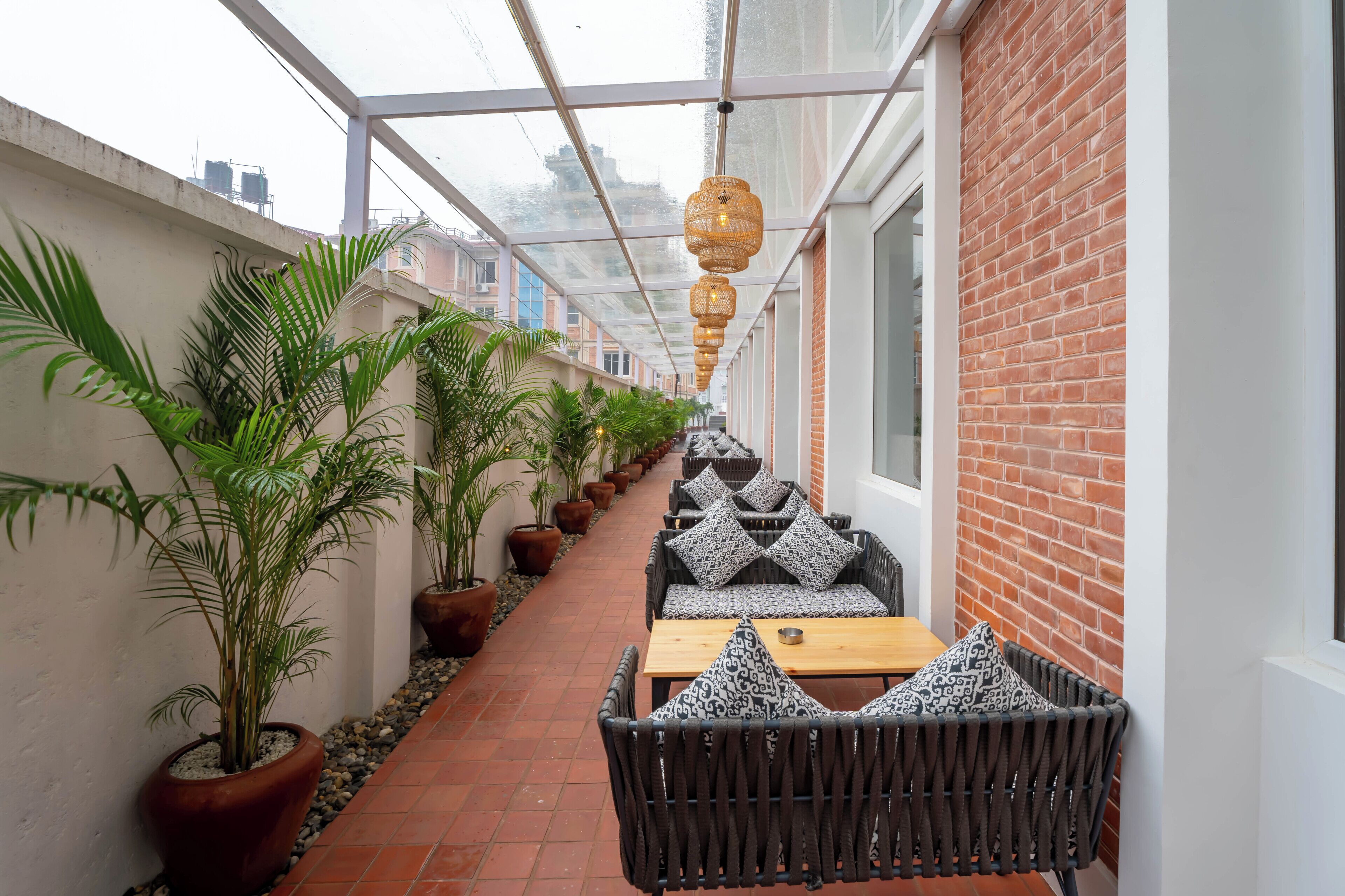 A covered outdoor seating area with potted plants, wicker furniture, and a brick wall.