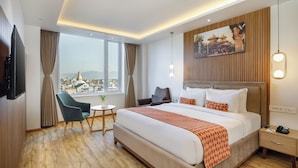 A hotel room with a large bed, a desk, a chair, a TV, and a window with a city view. - Hotel Anuttara, Boudha (Kathmandu)
