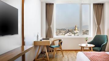A hotel room with a bed, a desk, a chair, a TV, and a window with a view of a cityscape and a bridge.
