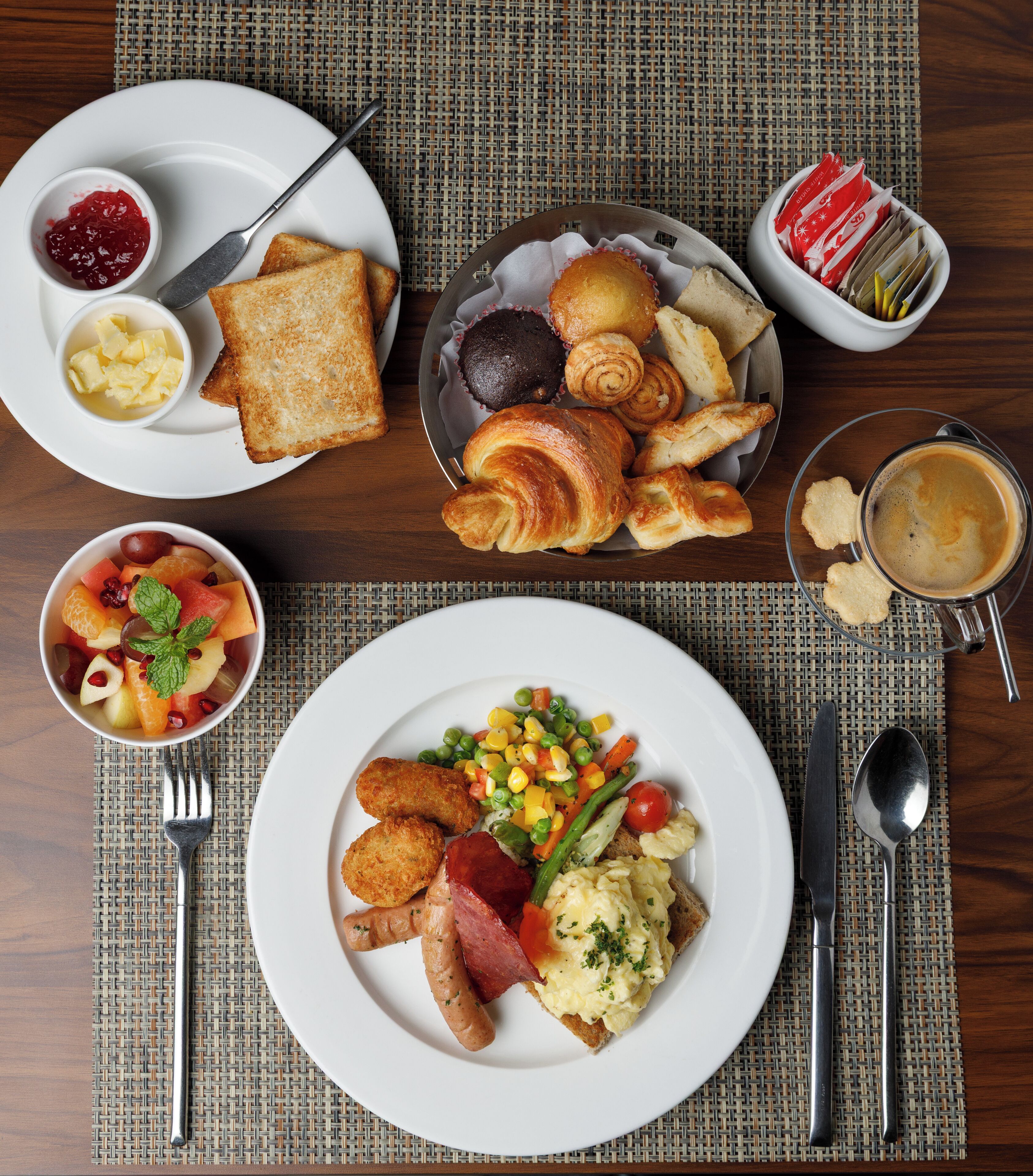 A breakfast setting with toast, croissants, muffins, and a fruit bowl.