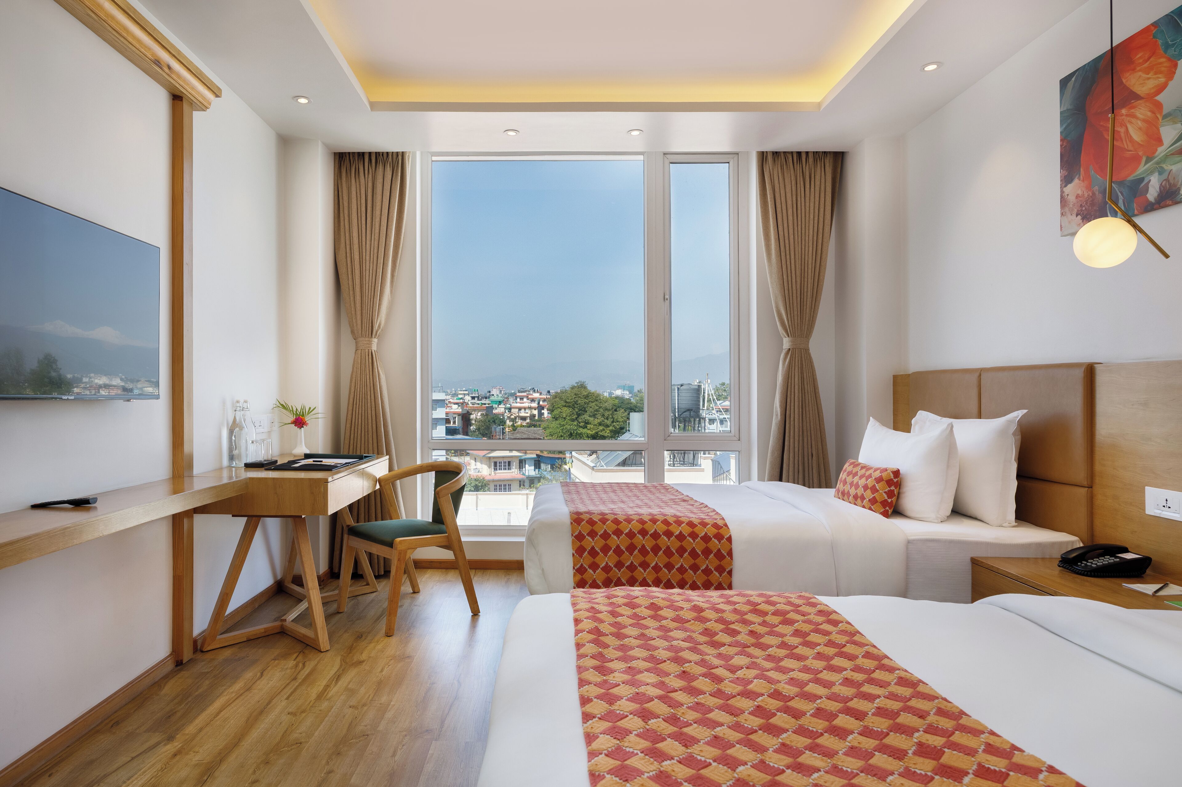 Una habitación de hotel con un ventanal grande, un escritorio, dos camas y una silla.