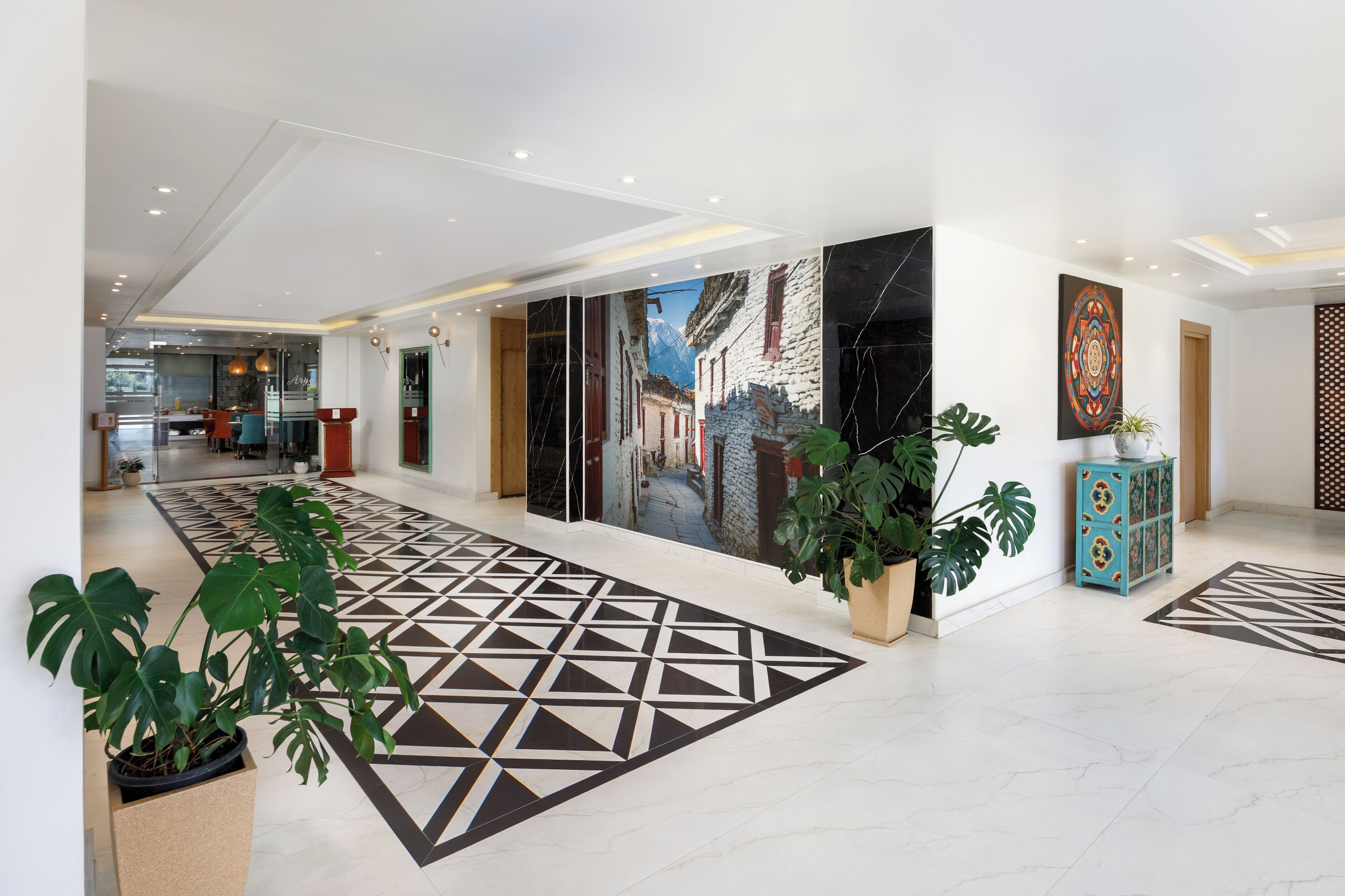 A modern hotel lobby with a geometric patterned floor, a mural of a street scene, and potted plants.