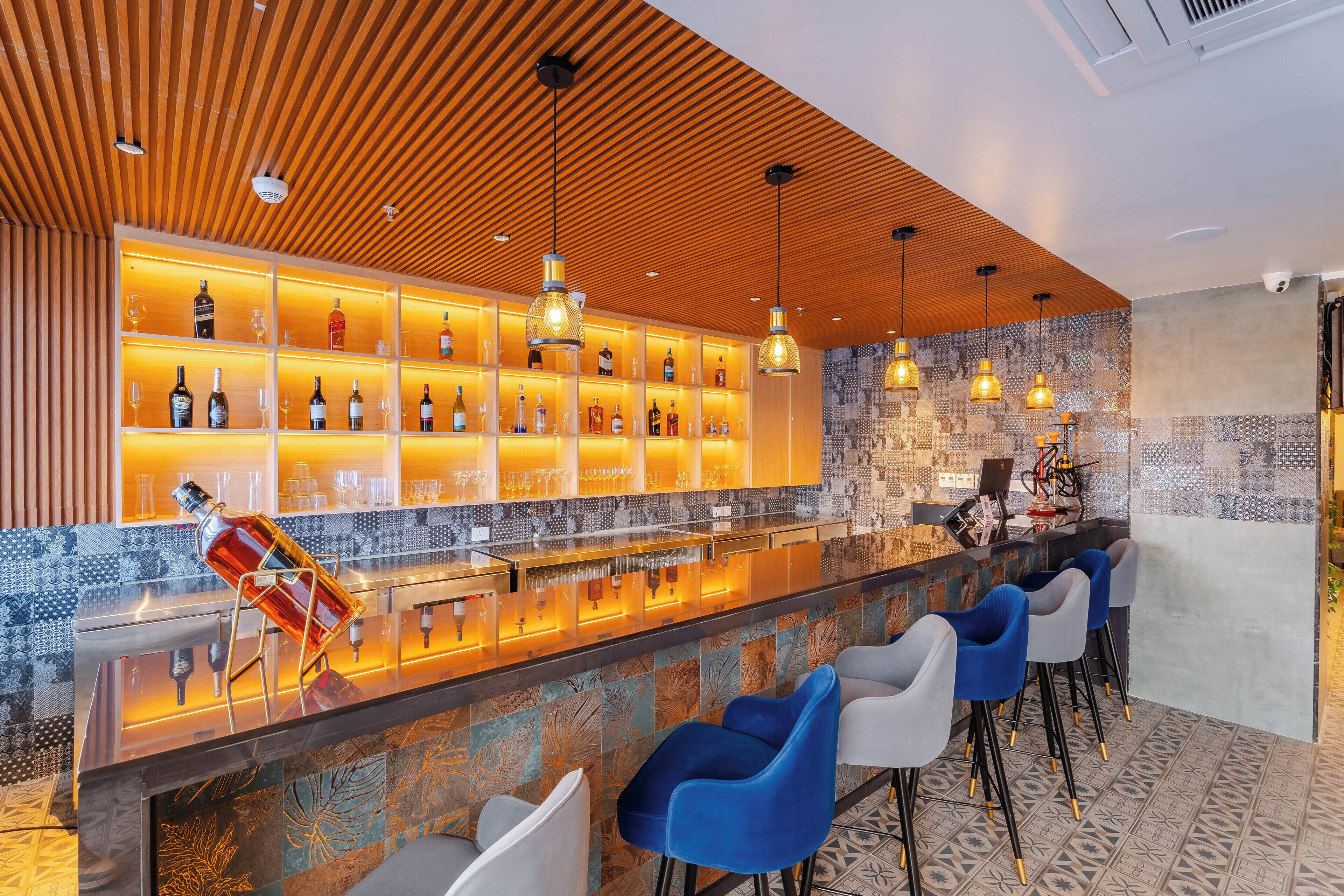 A bar area with a wooden ceiling, shelves with bottles, and bar stools.