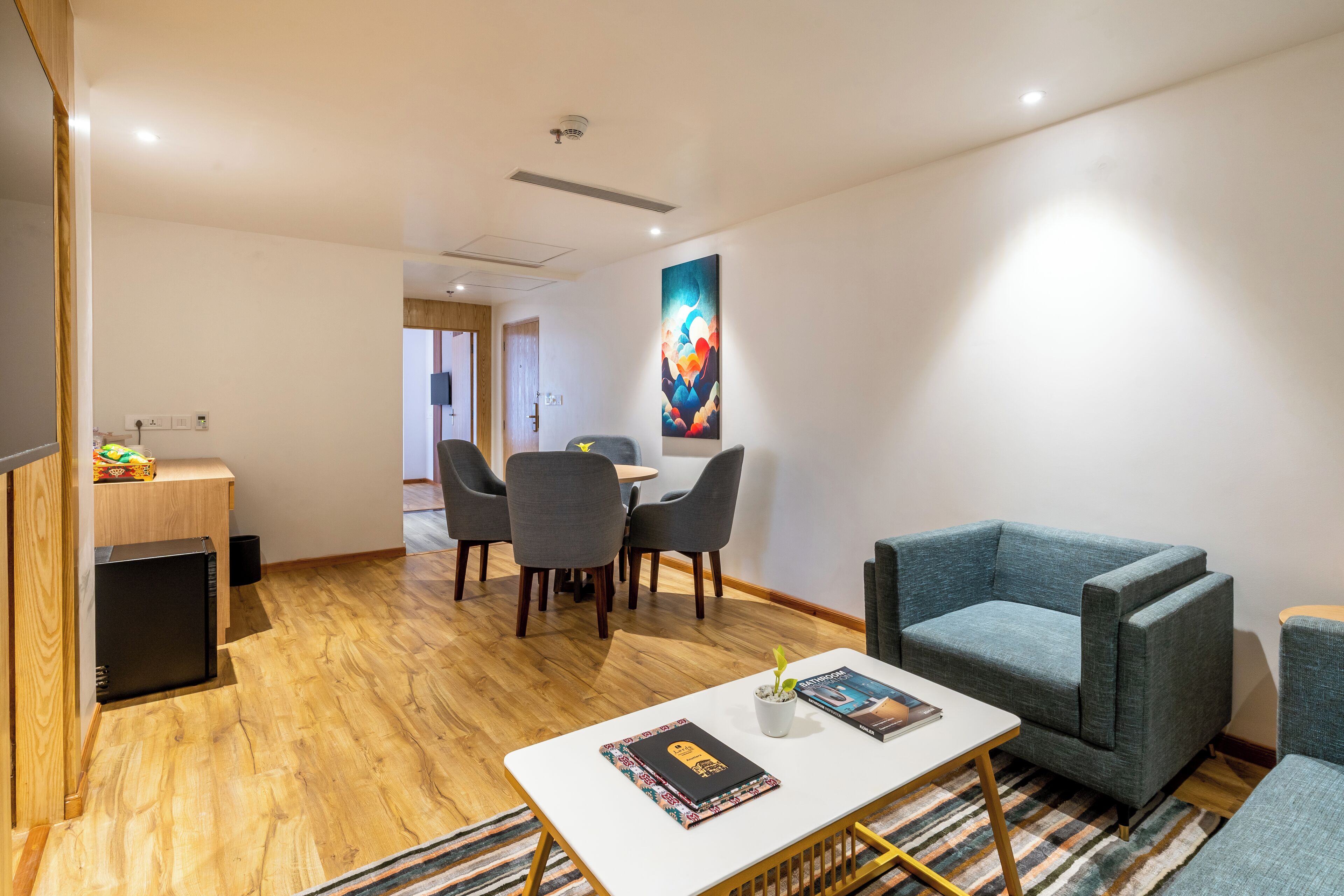 A modern living area with a dining table, chairs, a sofa, and a small table with a book and a plant.