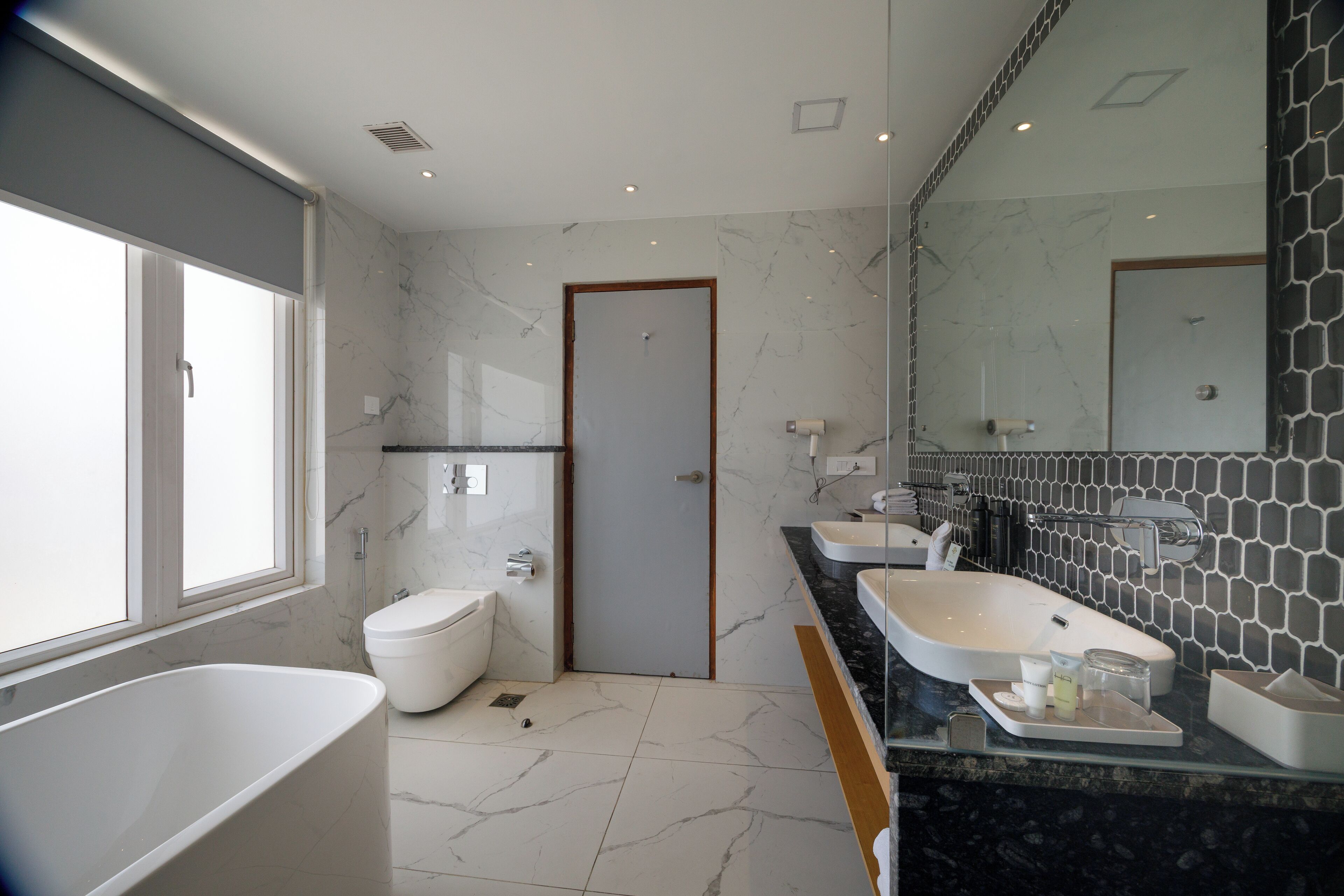 A modern bathroom with a large bathtub, two sinks, and a toilet.