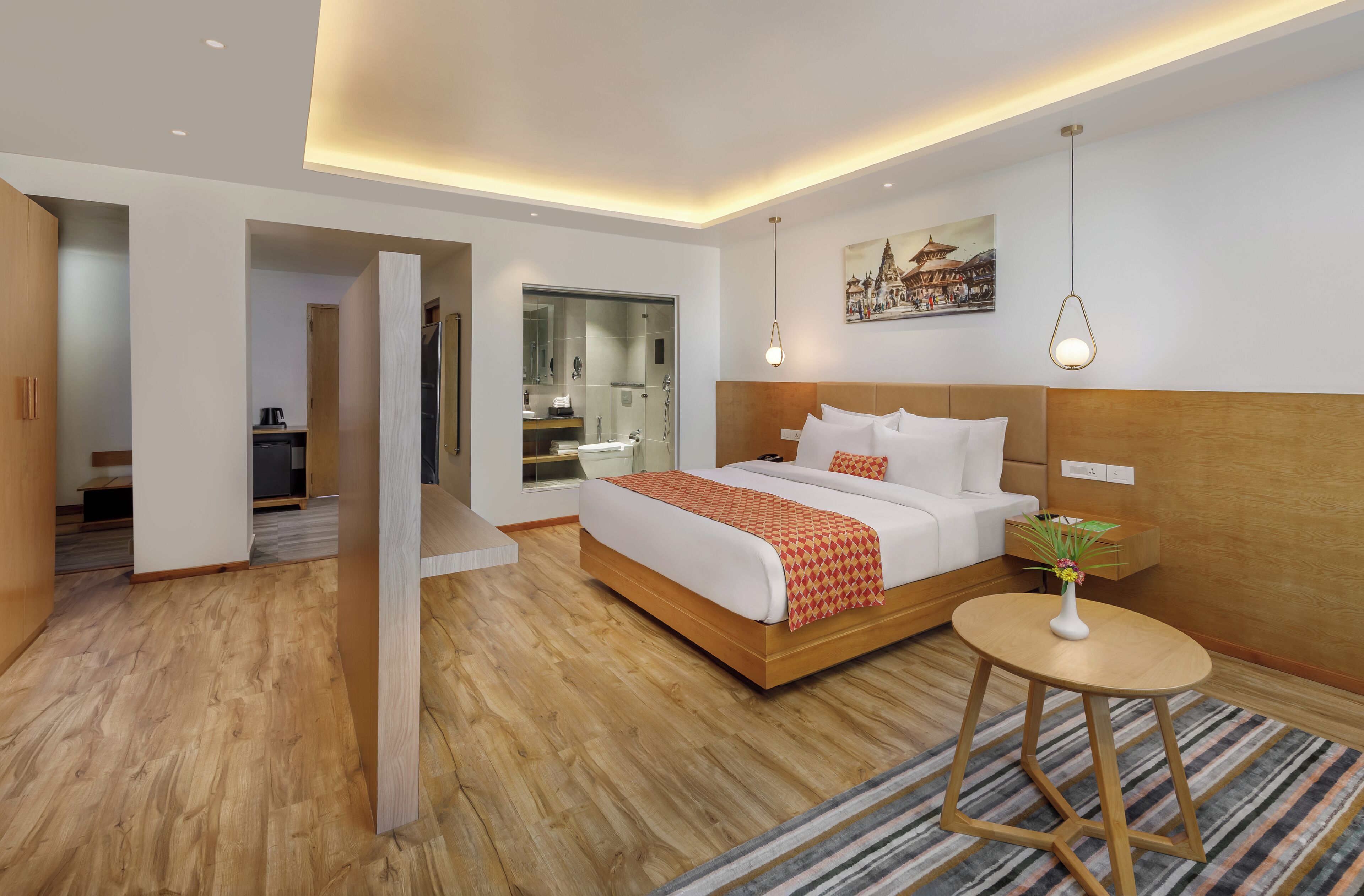 Habitació d'hotel moderna amb sòl de fusta, un llit gran amb col·cha vermella i blanca, una taula rodona petita amb un vas i un quadre d'un temple a la paret.
