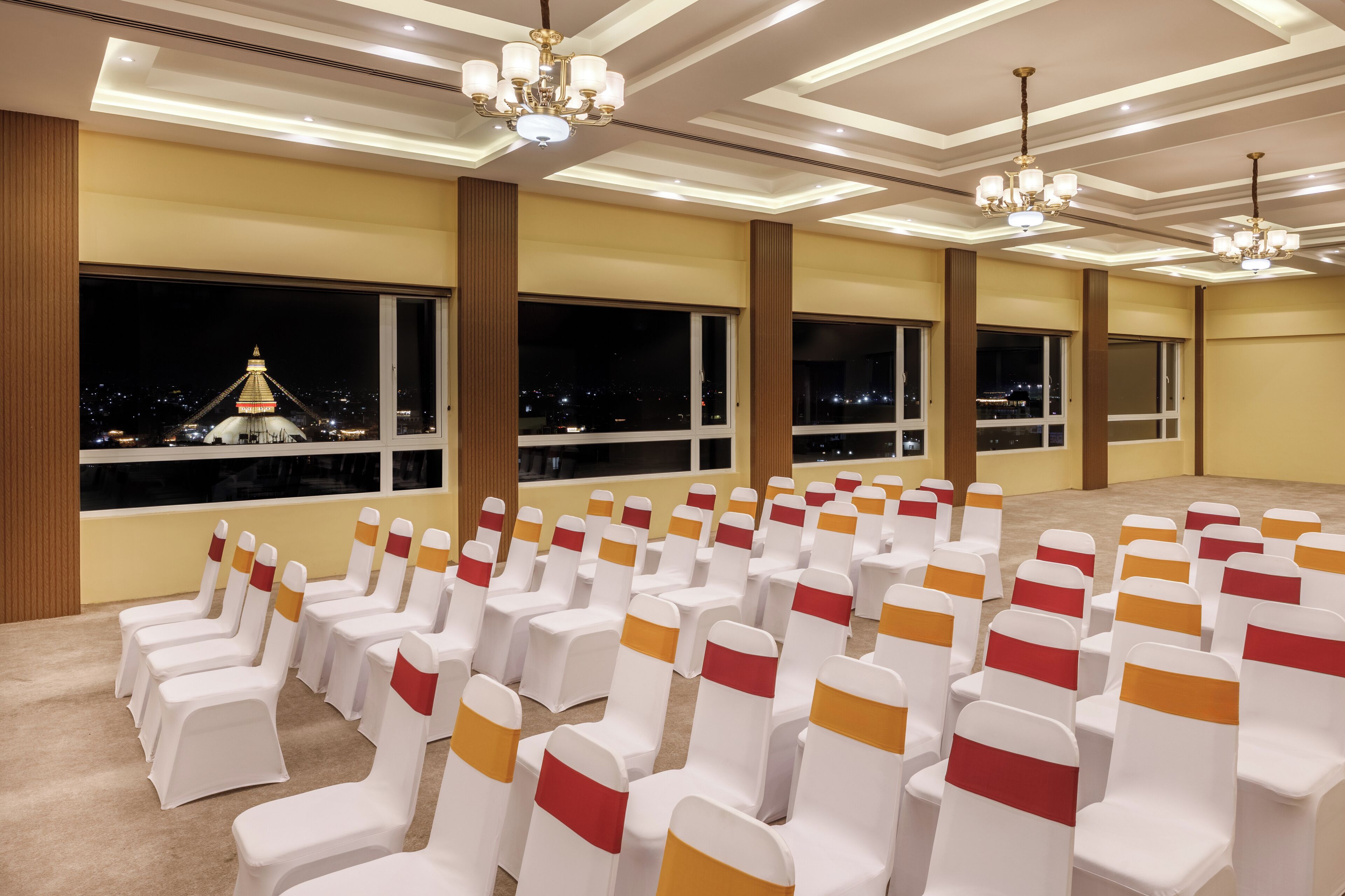 A conference room with rows of chairs, large windows, and chandeliers.