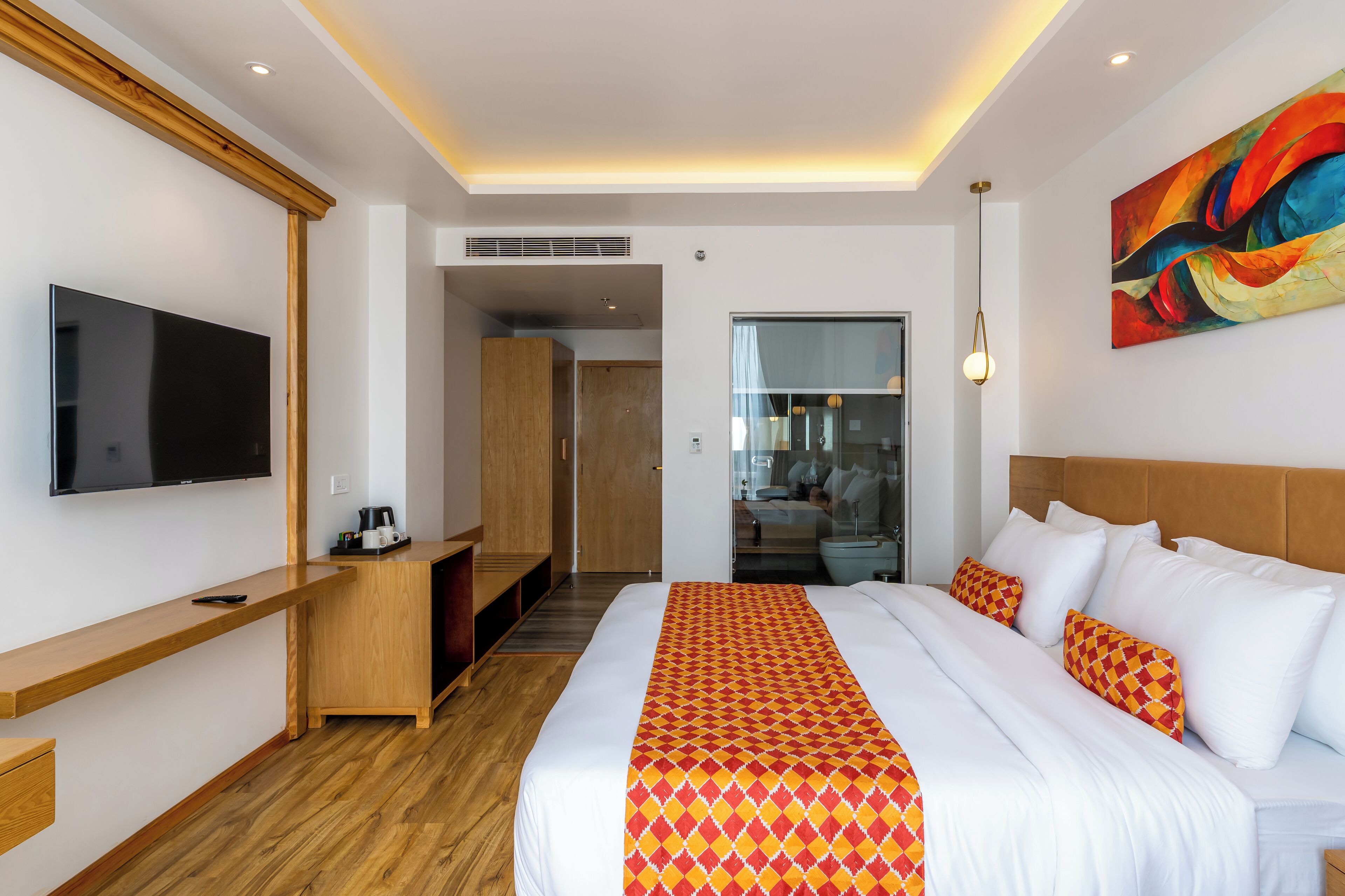A hotel room with a large bed, a TV mounted on the wall, a wooden desk, and a colorful painting on the wall.