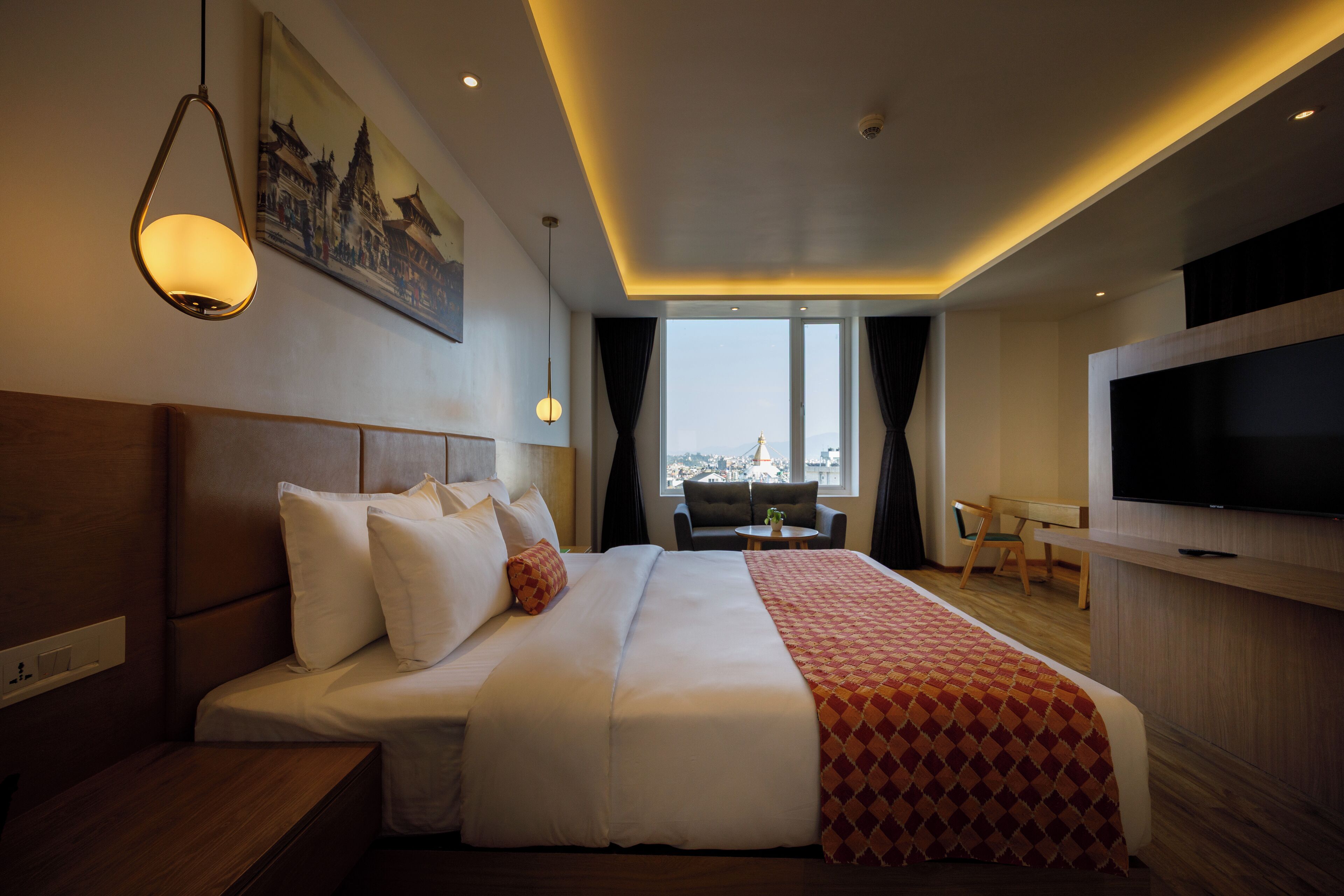 A hotel room with a large bed, a TV, a desk, and a view of the city through the window.