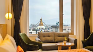 A hotel room with a large window offering a view of a cityscape and a prominent building with a golden spire. - Hotel Anuttara, Boudha (Kathmandu)