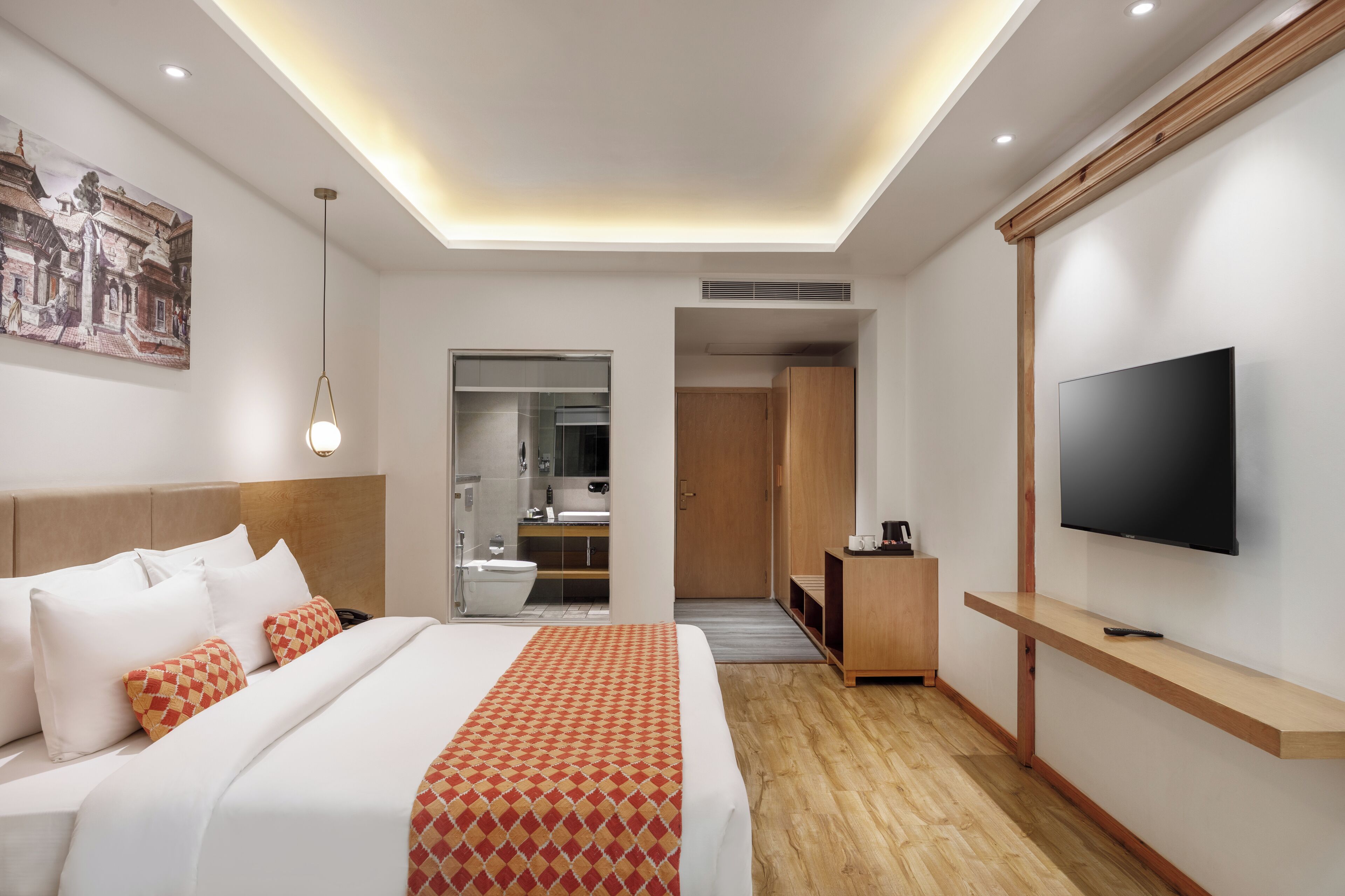 Habitación de hotel moderna con una cama grande, televisión, un aparador de madera y un baño visible a través de una puerta abierta.