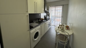 A compact kitchen with a washing machine, a sink, and a dining area with a table and chairs. - PEL1900 (Cannes)