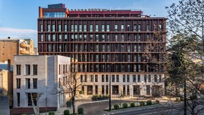 A multi-story building with a modern architectural design, featuring a mix of glass and metal facade, and a well-maintained surrounding area with a clear road and minimal landscaping. - Hotel Afisha (Tbilisi)