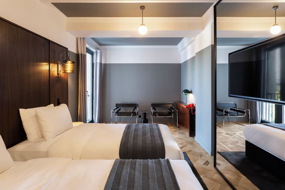 Habitación de hotel con una cama grande, un escritorio, dos sillas, un televisor y un espejo.