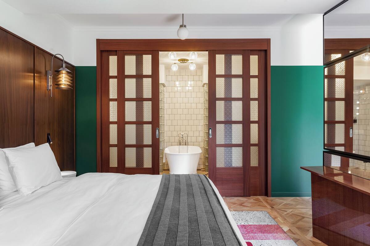 Un dormitorio con cama, mesita de noche, armario de madera, baño con bañera y espejo.