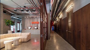 A modern hotel lobby with a large sectional sofa, a reception desk, and a wooden wall with louvered doors. - Hotel Afisha (Tbilisi)