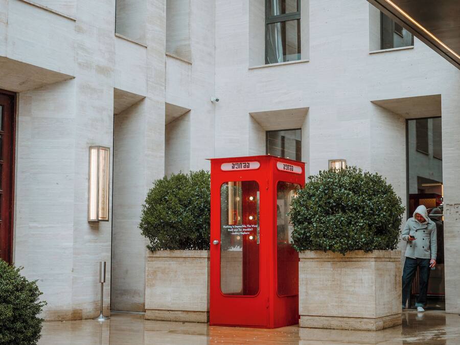 Un edificio moderno con una cabina telefónica roja, una escalera y una persona de pie cerca de la entrada.