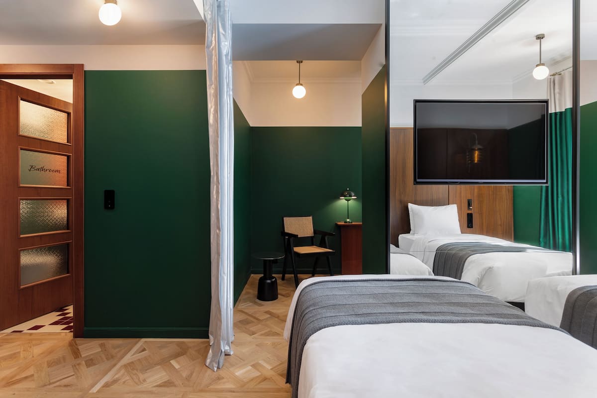 Habitación de hotel con dos camas, un televisor, una mesita con una silla y un letrero de baño.