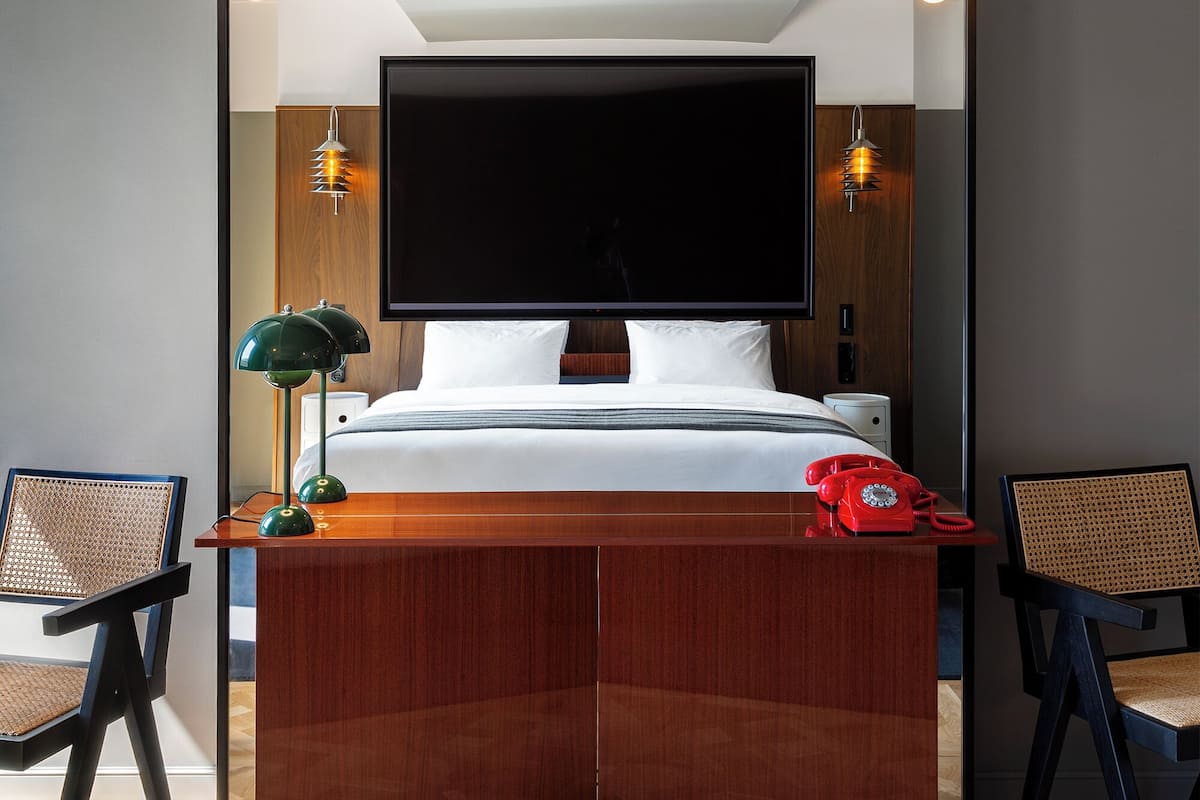 Una habitación de hotel moderna con una cama grande, un televisor de pantalla plana, un escritorio de madera, dos sillas y un teléfono.