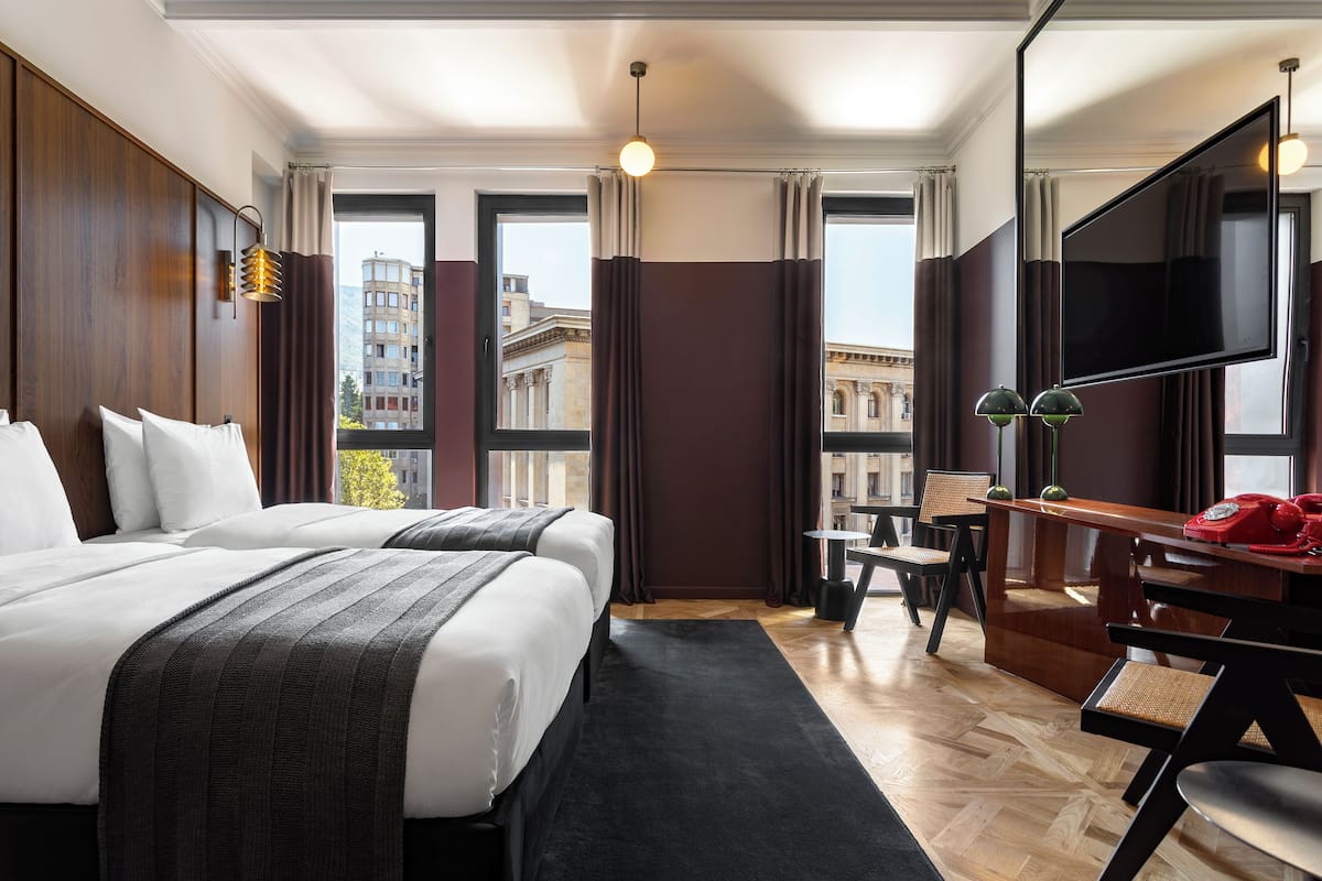 Habitación de hotel con dos camas, un escritorio con teléfono, una silla y un televisor.