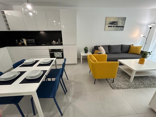 Un salon moderne comprenant un canapé, une table à manger avec des chaises et un coin cuisine avec des placards et des appareils électroménagers.