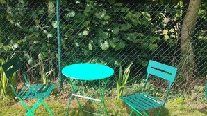Un set tavolo e sedia in metallo verde, con una recinzione a maglie metalliche e vegetazione sullo sfondo.