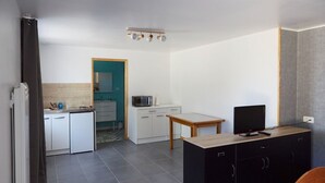 Un ambiente compatto con angolo cottura, zona pranzo e TV su un mobile.