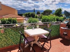 A balcony with a table and chairs, potted plants, and a view of mountains and trees.
