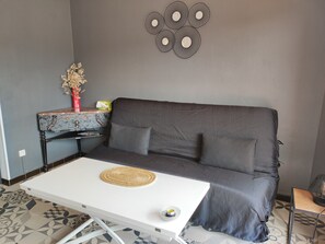 A modern living room with a grey sofa, a white coffee table, a decorative wall piece, and a small side table with a vase of flowers.