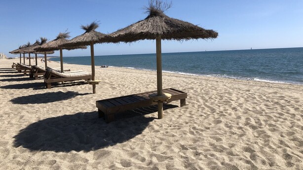 A beach with thatched umbrellas and wooden lounge chairs.