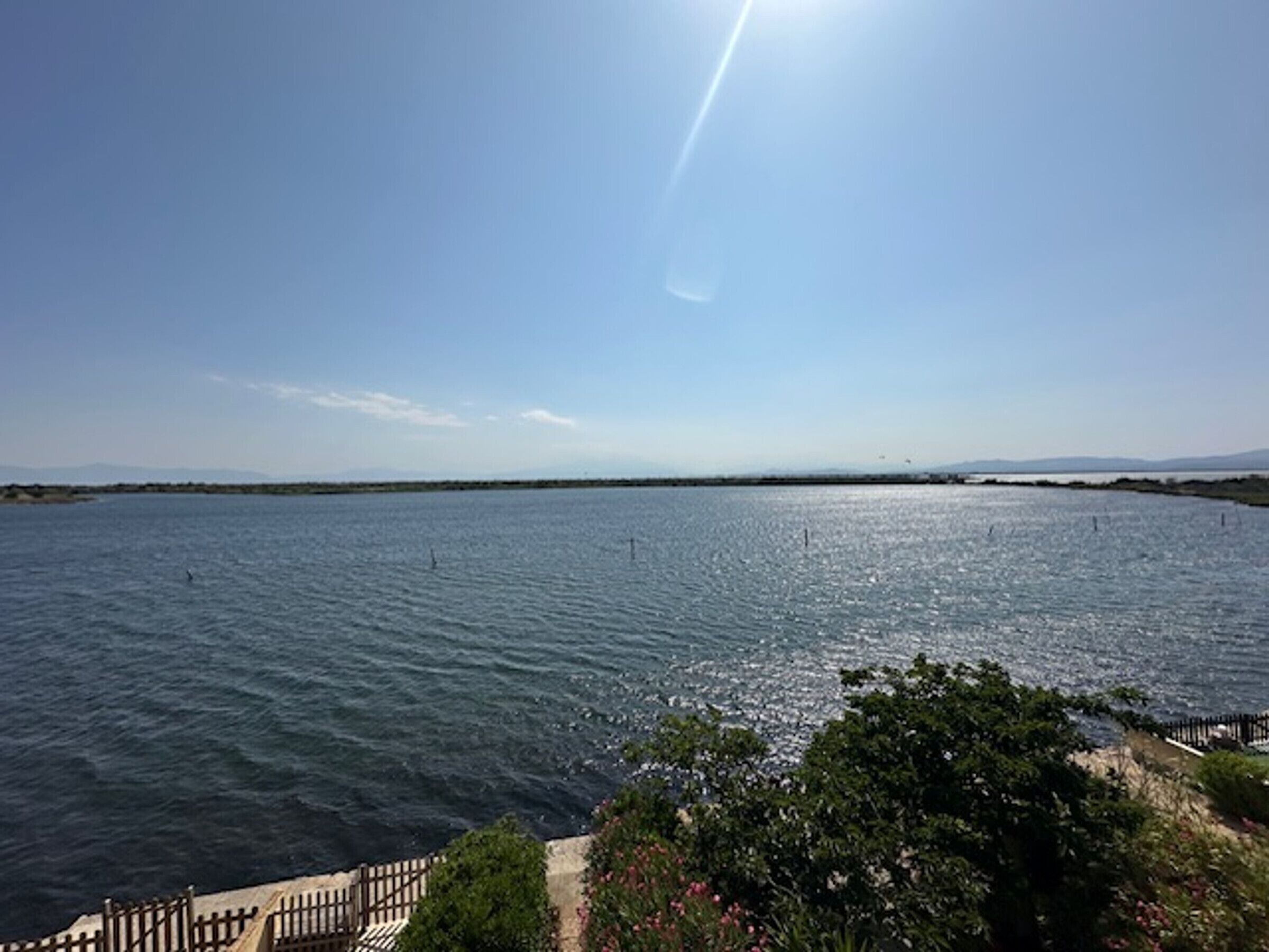 A coastal view with a clear sky, calm sea, and a wooden walkway leading to the water.