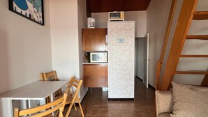 A compact kitchen with a microwave, a coffee maker, and a refrigerator. There is a dining table with chairs and a sofa in the living area. - Mezzanine Studio 4P with View, Private Parking - Le Barcarès (Le Barcarès)
