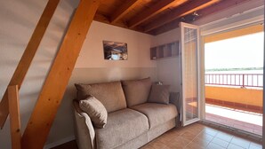 A cozy room with a wooden ceiling, a beige sofa, and a sliding glass door leading to an outdoor balcony. - Mezzanine Studio 4P with View, Private Parking - Le Barcarès (Le Barcarès)
