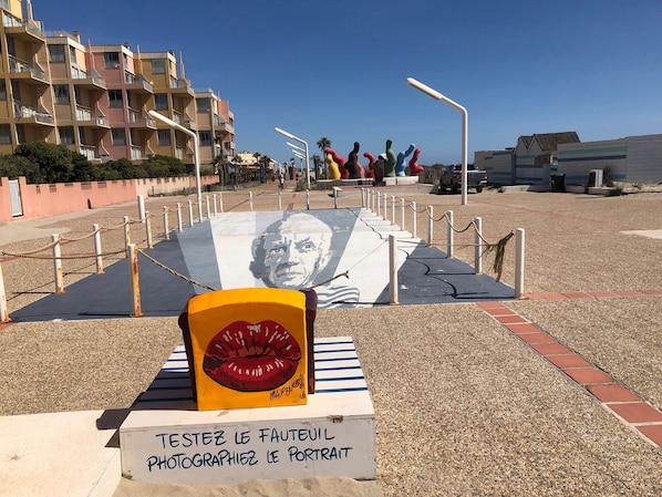 Calle con un mural grande de un rostro masculino, un objeto amarillo con labios y un letrero en francés.