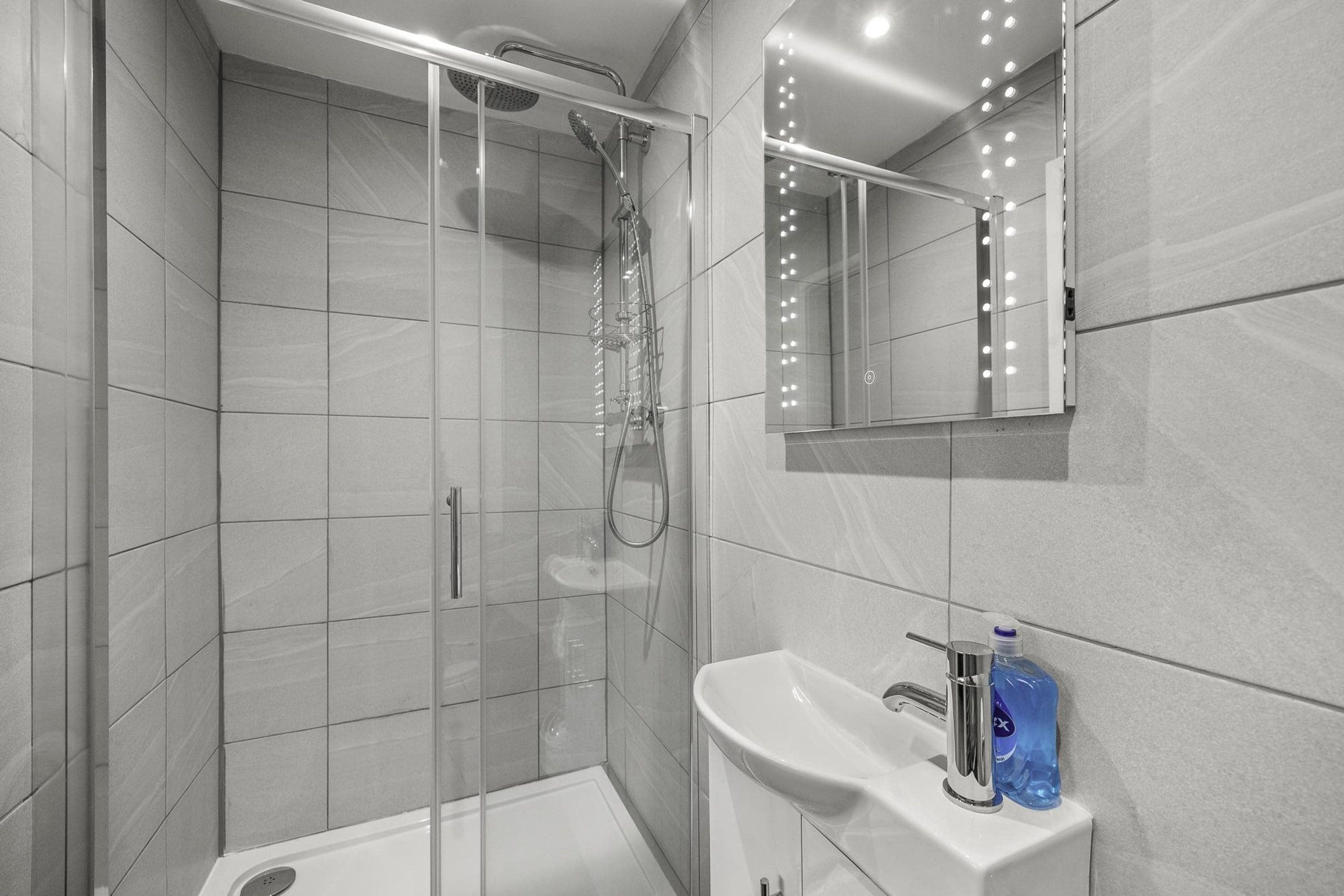 A modern bathroom with a glass-enclosed shower, a white sink, and a mirror with lights.