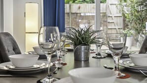 A dining table set with white bowls, plates, and silverware, accompanied by wine glasses and a potted plant. - Sunset Townhouse With Free Parking (Brighton)