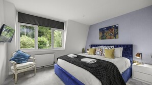 A bedroom with a large bed, a chair, a nightstand, a TV, and a window with a view of greenery. - Sunset Townhouse With Free Parking (Brighton)
